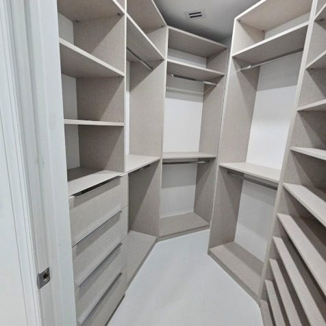 Walk-in closet with custom white shelving, hanging sections and drawer banks